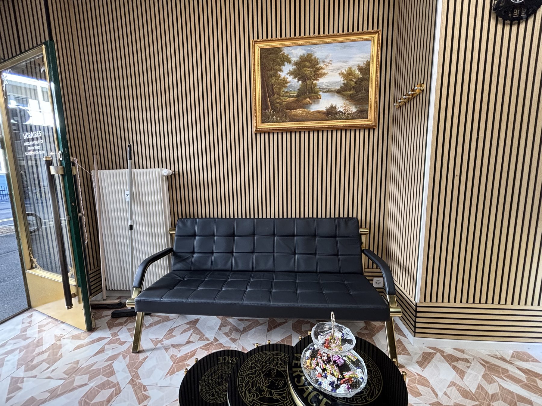 Le coin d'attente du salon : canapé noir, table dorée, tableau et tasseaux de bois